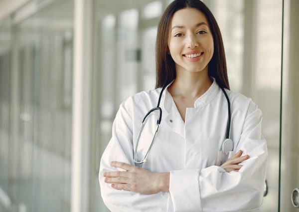 Portrait of a smiling female doctor with arms crossed and stethoscope in a hospital corridor.